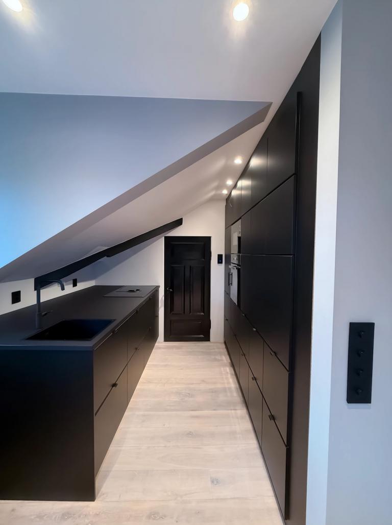 Arealeffektivt kjøkken med integrerte hvitevarer og stor benkeplate for enkel matlaging.